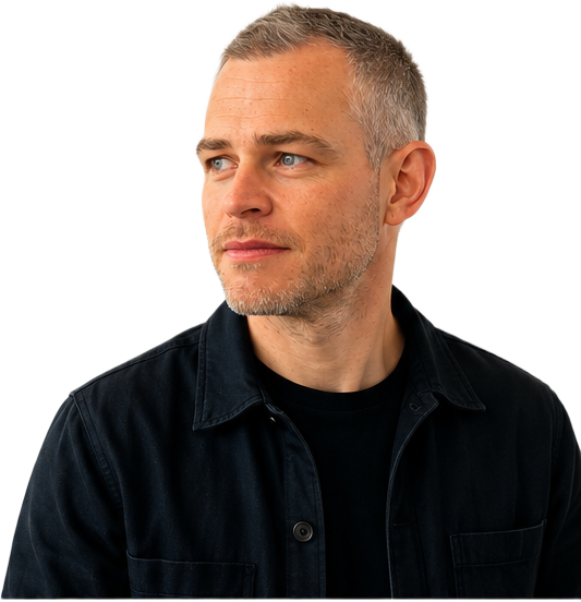 Tom Sharp, wearing a dark overshirt over a black t-shirt, turned slightly towards the page.